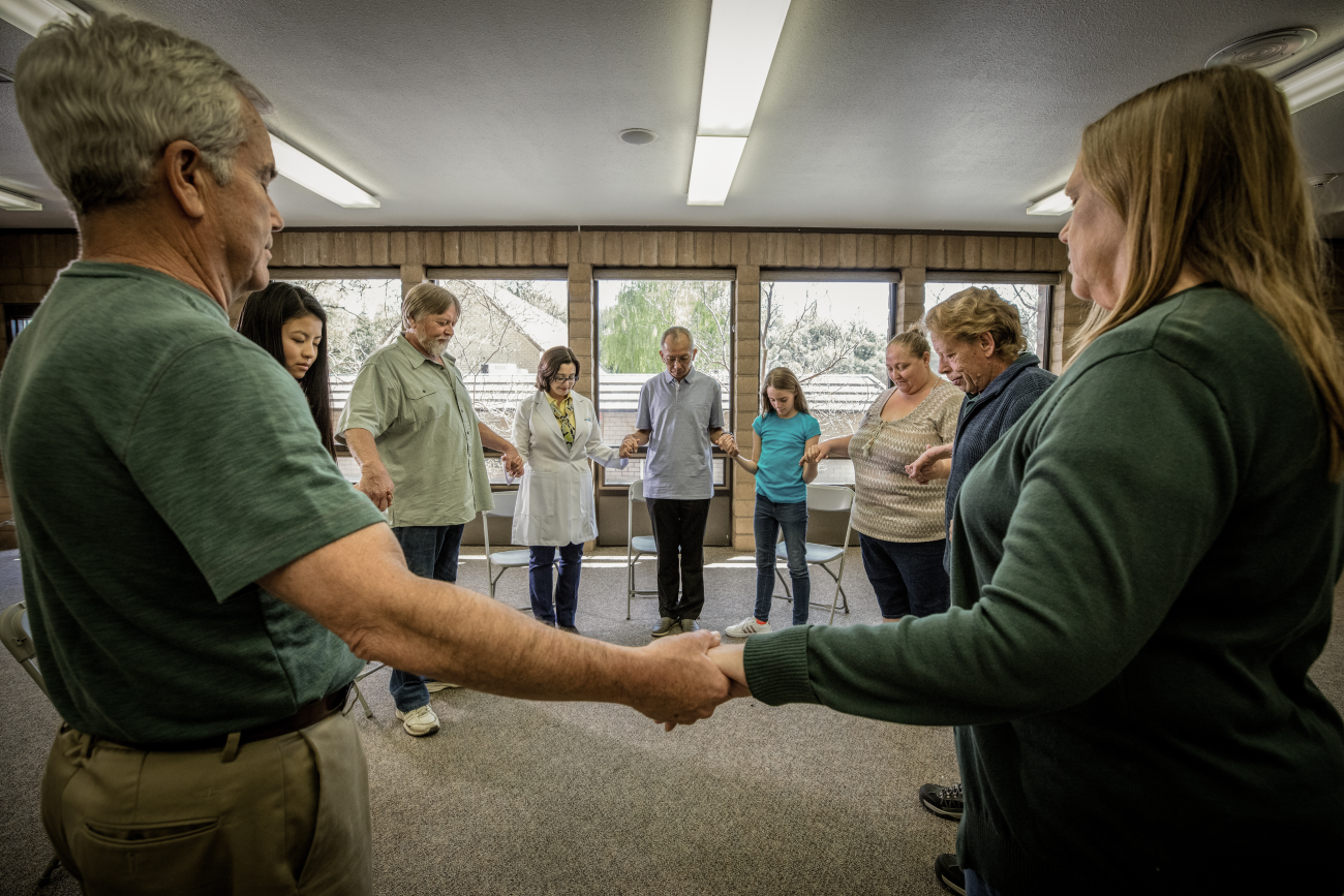 Nine people are standing in a circle holding hands indoors